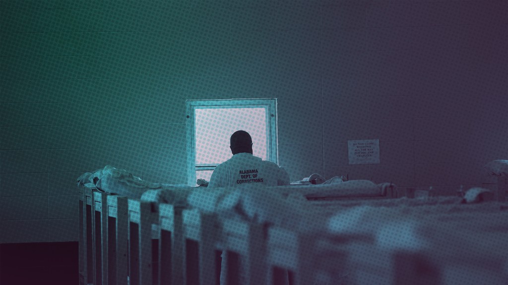 Blue tinted photo of a man staring out of a window in an Alabama prison wearing an Alabama department of Corrections shirt in a room with bunkbeds.